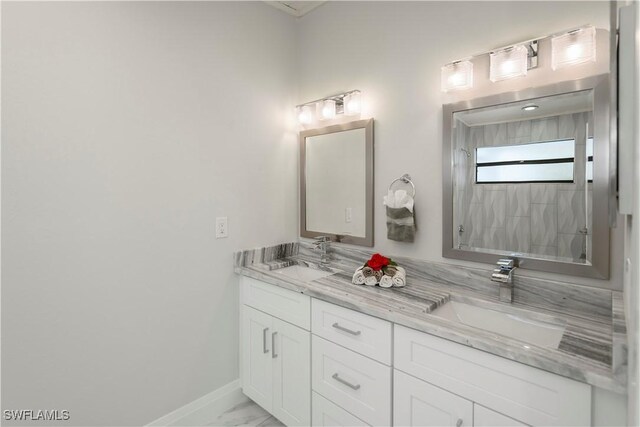 bathroom with marble finish floor, double vanity, a sink, and baseboards