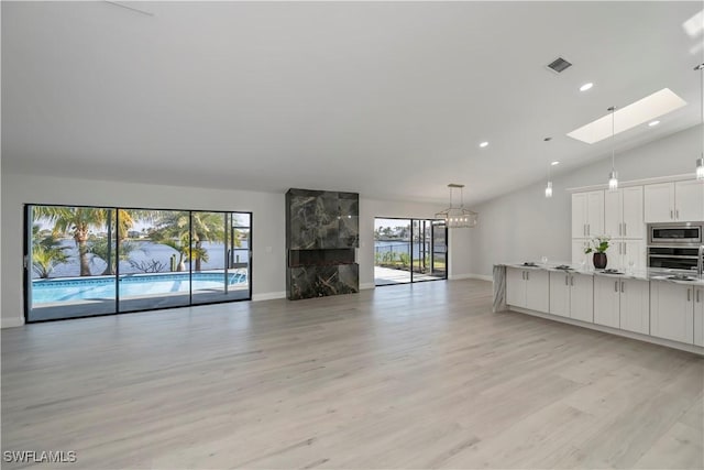 unfurnished living room with light wood finished floors, recessed lighting, visible vents, vaulted ceiling with skylight, and baseboards