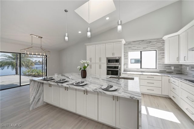 kitchen featuring light stone counters, white cabinetry, appliances with stainless steel finishes, tasteful backsplash, and pendant lighting