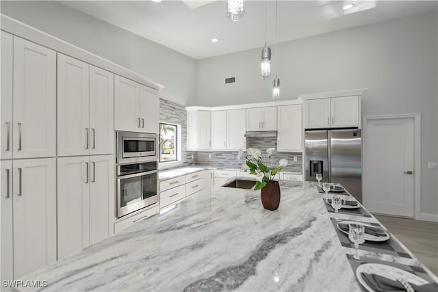 kitchen featuring appliances with stainless steel finishes, decorative light fixtures, light stone countertops, white cabinetry, and a sink