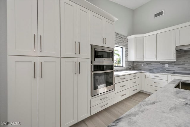 kitchen with tasteful backsplash, visible vents, light stone counters, stainless steel appliances, and white cabinetry