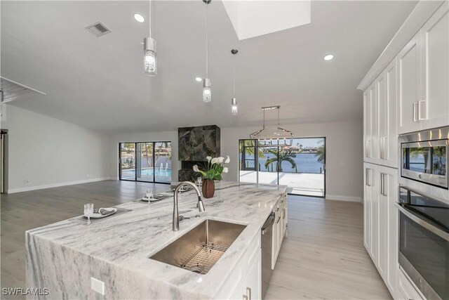 kitchen featuring light stone counters, stainless steel appliances, visible vents, white cabinets, and a sink