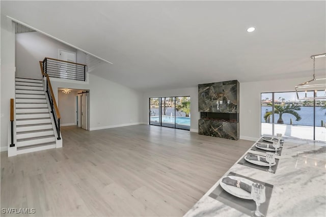 unfurnished living room featuring vaulted ceiling, stairway, baseboards, and wood finished floors