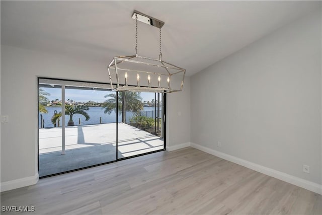 unfurnished dining area featuring vaulted ceiling, a water view, wood finished floors, and baseboards