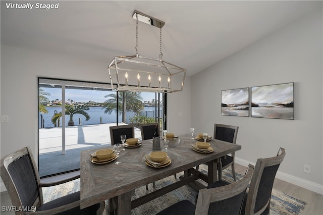 dining space with a water view, vaulted ceiling, baseboards, and wood finished floors