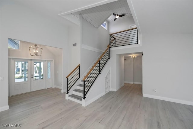 foyer entrance featuring french doors, a high ceiling, wood finished floors, a chandelier, and stairs