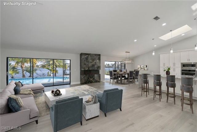 living room with light wood-type flooring, lofted ceiling with skylight, visible vents, and recessed lighting