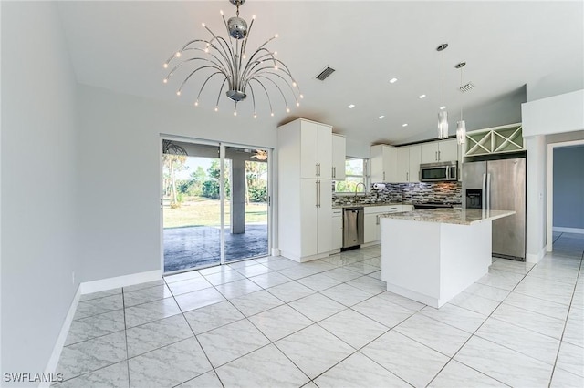 kitchen with stainless steel appliances, a kitchen island, backsplash, pendant lighting, and white cabinets