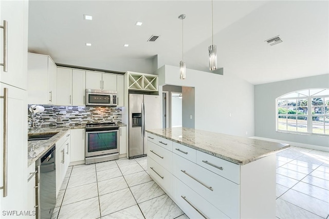 kitchen featuring lofted ceiling, white cabinets, decorative backsplash, appliances with stainless steel finishes, and a kitchen island