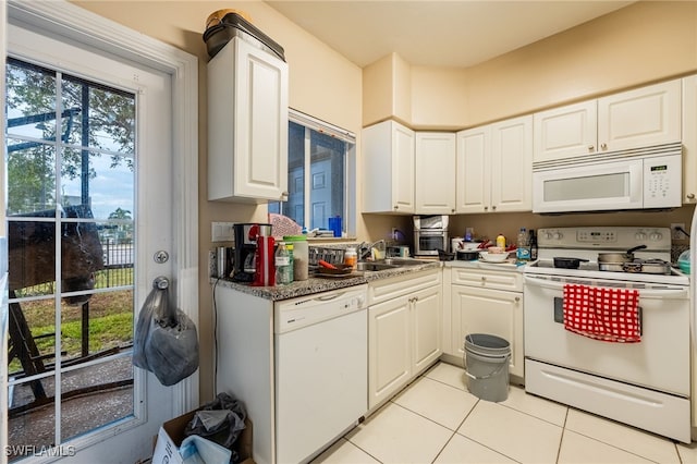 kitchen featuring dark stone countertops, sink, white appliances, white cabinetry, and light tile patterned floors