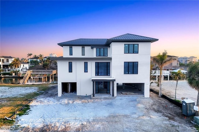 view of front of property featuring metal roof, a water view, stucco siding, driveway, and a carport