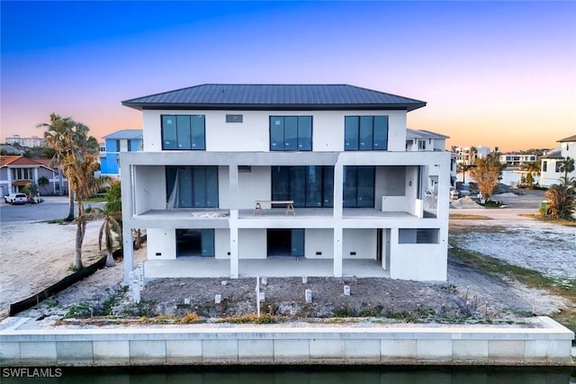 back of property at dusk featuring a balcony, metal roof, stucco siding, and a patio area