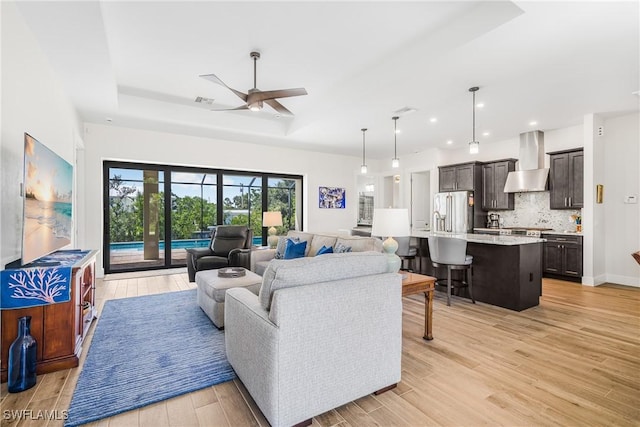 living room with light wood-type flooring, a tray ceiling, and ceiling fan