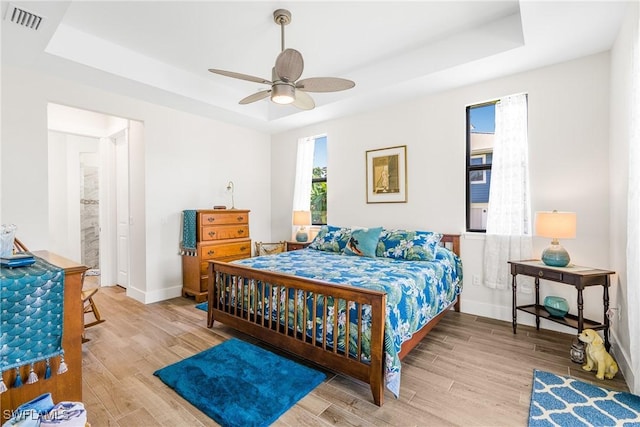 bedroom with ceiling fan, a raised ceiling, and light hardwood / wood-style flooring