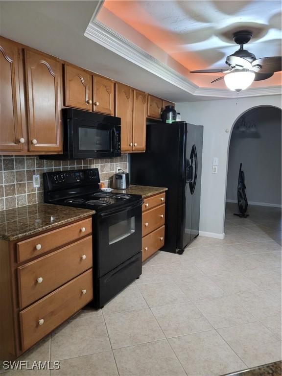 kitchen featuring tasteful backsplash, a raised ceiling, dark stone countertops, and black appliances