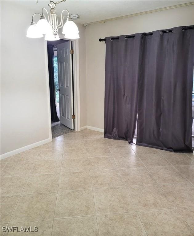 tiled spare room featuring a chandelier