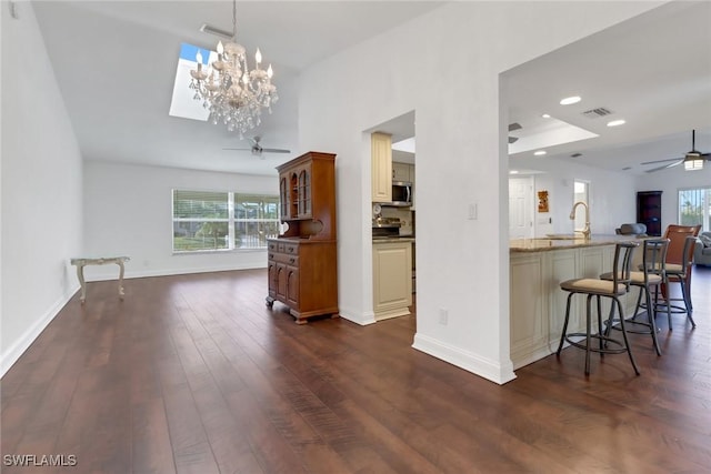 kitchen featuring sink, dark wood-type flooring, dark stone countertops, decorative light fixtures, and a breakfast bar area