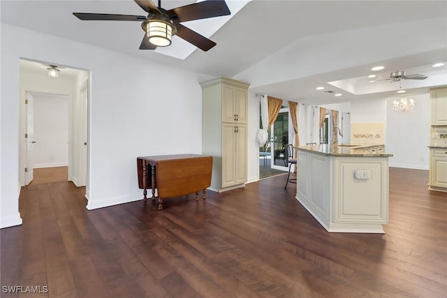 kitchen featuring sink, dark hardwood / wood-style floors, light stone countertops, an island with sink, and cream cabinetry