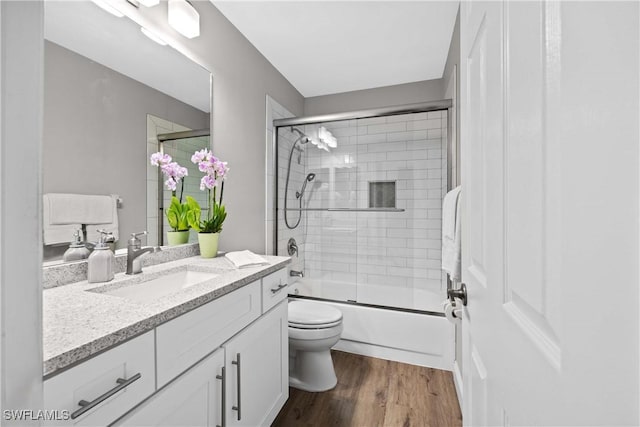 full bathroom with shower / bath combination with glass door, hardwood / wood-style floors, vanity, and toilet