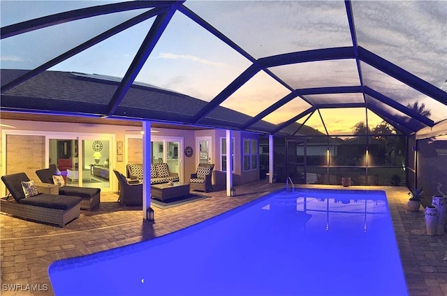 pool at dusk featuring outdoor lounge area, glass enclosure, and a patio