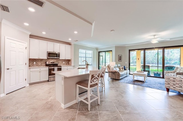 kitchen with ceiling fan, sink, stainless steel appliances, an island with sink, and white cabinets