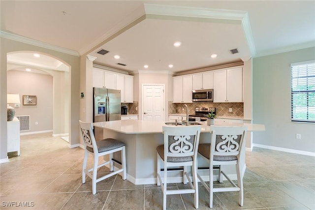 kitchen with white cabinets, stainless steel appliances, a breakfast bar area, and an island with sink