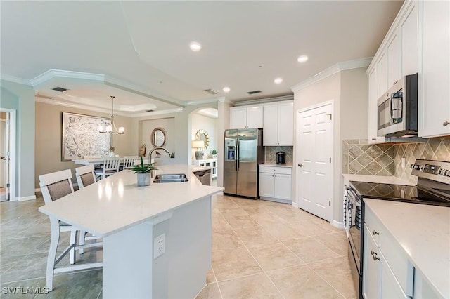 kitchen with a kitchen island with sink, stainless steel appliances, a kitchen breakfast bar, decorative backsplash, and white cabinets