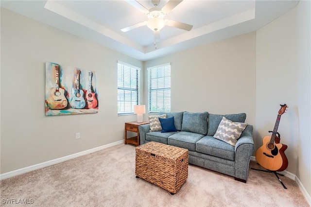 carpeted living room with ceiling fan and a tray ceiling