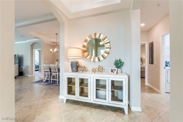 hallway with washer / dryer, an inviting chandelier, and crown molding