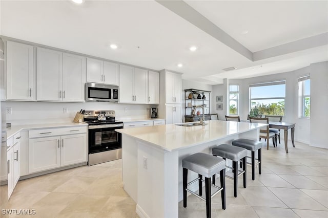 kitchen featuring sink, white cabinetry, stainless steel appliances, and an island with sink