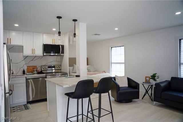 kitchen with light stone countertops, appliances with stainless steel finishes, decorative backsplash, white cabinets, and hanging light fixtures