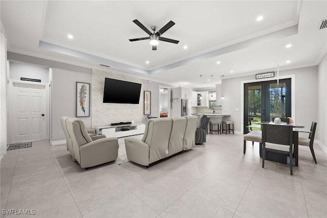 living room featuring ceiling fan, french doors, a raised ceiling, light tile patterned flooring, and ornamental molding