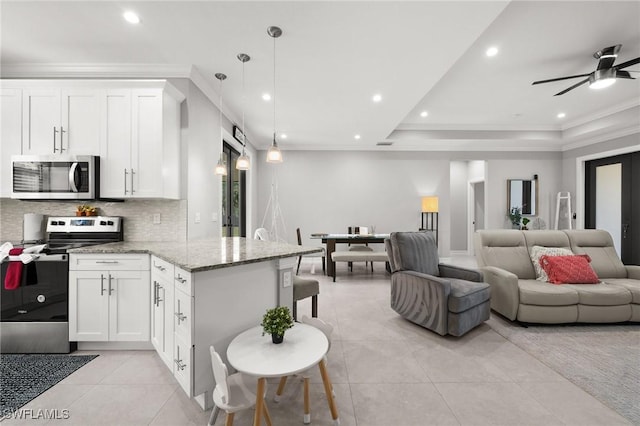 kitchen featuring hanging light fixtures, stainless steel appliances, light stone counters, a tray ceiling, and white cabinets