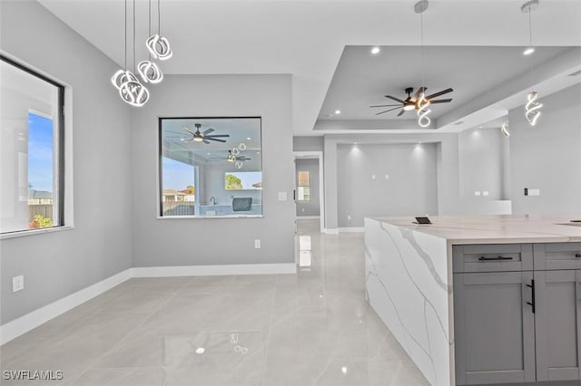 kitchen with a tray ceiling, gray cabinetry, light stone countertops, and pendant lighting