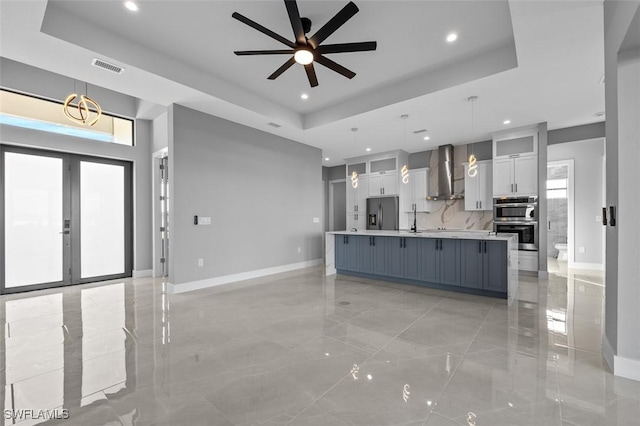 kitchen featuring wall chimney exhaust hood, hanging light fixtures, a large island with sink, white cabinets, and appliances with stainless steel finishes