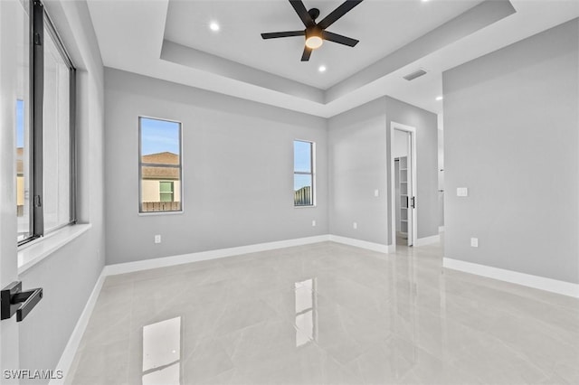 empty room with ceiling fan and a tray ceiling