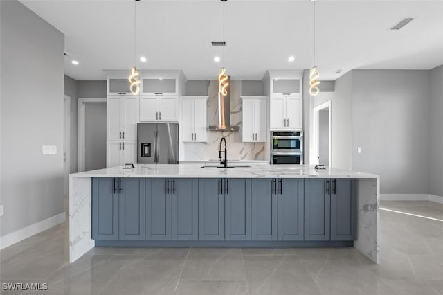 kitchen with white cabinetry, wall chimney exhaust hood, a large island with sink, decorative light fixtures, and appliances with stainless steel finishes