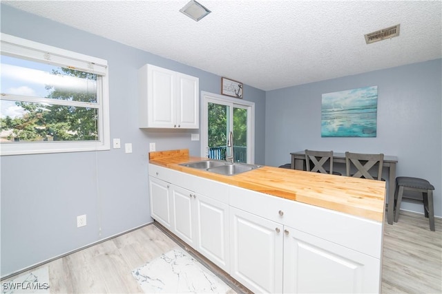 kitchen with wooden counters, a textured ceiling, white cabinetry, and sink