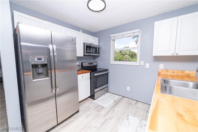 kitchen featuring butcher block countertops, white cabinets, stainless steel appliances, and a textured ceiling