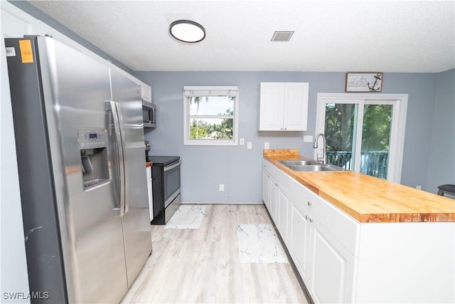 kitchen featuring a textured ceiling, white cabinetry, stainless steel appliances, and wooden counters