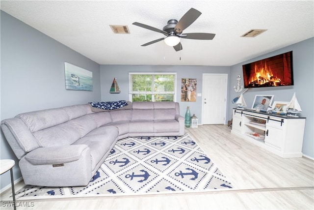 living room with ceiling fan, light hardwood / wood-style flooring, and a textured ceiling