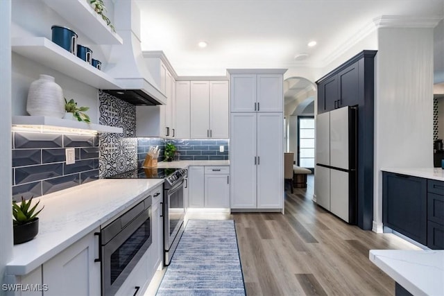 kitchen with light hardwood / wood-style floors, premium range hood, white cabinets, stainless steel appliances, and light stone counters