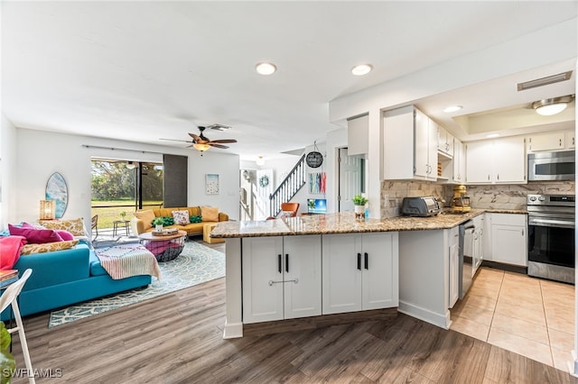 kitchen with kitchen peninsula, stainless steel appliances, white cabinets, and light stone countertops