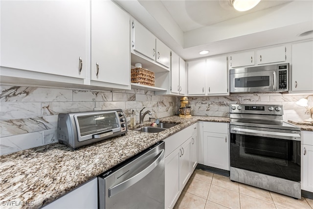 kitchen with appliances with stainless steel finishes, tasteful backsplash, sink, light tile patterned floors, and white cabinets