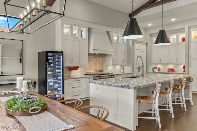 kitchen featuring light stone counters, white cabinetry, custom range hood, and an island with sink