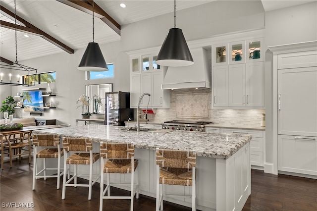 kitchen featuring white cabinets, an island with sink, pendant lighting, and vaulted ceiling with beams