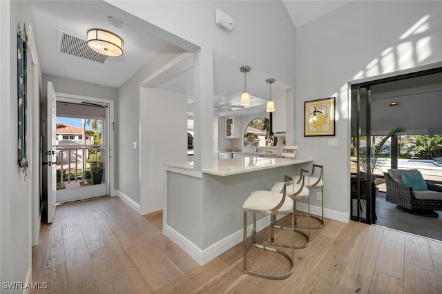 interior space with light wood-style floors, visible vents, a peninsula, and a breakfast bar area