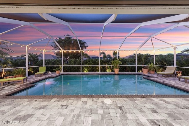 pool at dusk with a patio area, a mountain view, and glass enclosure