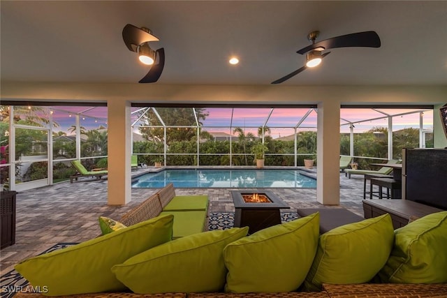 pool at dusk featuring a lanai, an outdoor living space with a fire pit, a patio area, and ceiling fan