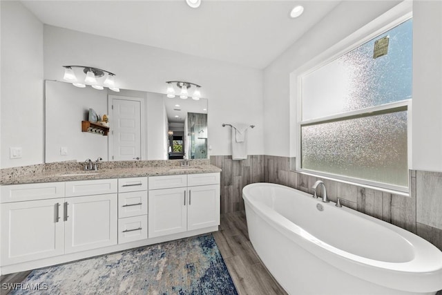 bathroom with a tub to relax in, plenty of natural light, vanity, and hardwood / wood-style flooring